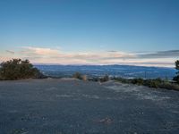 the view looking out over a wide valley below the mountains at twilight, from a large hill with a bench on top