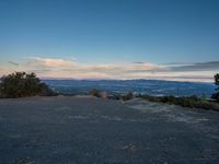 the view looking out over a wide valley below the mountains at twilight, from a large hill with a bench on top