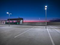 a commercial warehouse sits empty in this empty parking lot at night time at twilight with lights in the foreground