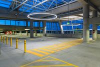 a view of an open parking lot at twilight with yellow lines on the ground, a streetlight and some pillars