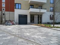 two bikes are parked against a row of residential buildings in a city driveway with brick pavers on the ground