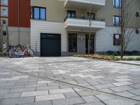 two bikes are parked against a row of residential buildings in a city driveway with brick pavers on the ground