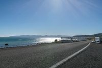 two buses parked by the beach on the side of a road with water in front