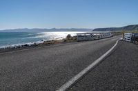 two buses parked by the beach on the side of a road with water in front