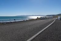 two buses parked by the beach on the side of a road with water in front