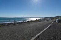 two buses parked by the beach on the side of a road with water in front