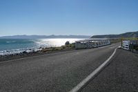 two buses parked by the beach on the side of a road with water in front