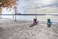 two park chairs sit on the side of the water by the river shore in fall