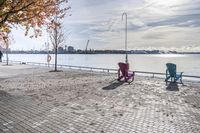 two park chairs sit on the side of the water by the river shore in fall