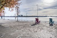 two park chairs sit on the side of the water by the river shore in fall