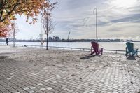 two park chairs sit on the side of the water by the river shore in fall