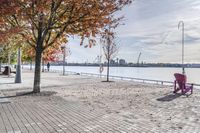 two park chairs sit on the side of the water by the river shore in fall