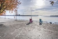 two park chairs sit on the side of the water by the river shore in fall