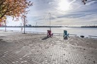 two park chairs sit on the side of the water by the river shore in fall