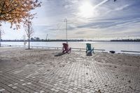 two park chairs sit on the side of the water by the river shore in fall