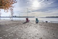 two park chairs sit on the side of the water by the river shore in fall