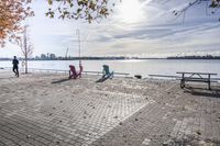 two park chairs sit on the side of the water by the river shore in fall