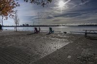 two park chairs sit on the side of the water by the river shore in fall