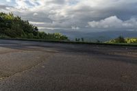 an empty asphalt road with a mountain in the distance and clouds in the sky overhead