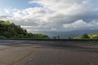 an empty asphalt road with a mountain in the distance and clouds in the sky overhead