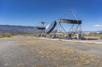 two very large satellite antennas with mountains in the background in a desert area by an open space road