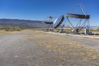 two very large satellite antennas with mountains in the background in a desert area by an open space road