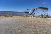 two very large satellite antennas with mountains in the background in a desert area by an open space road