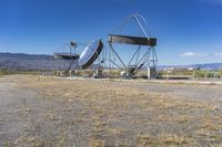 two very large satellite antennas with mountains in the background in a desert area by an open space road