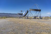 two very large satellite antennas with mountains in the background in a desert area by an open space road