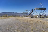 two very large satellite antennas with mountains in the background in a desert area by an open space road