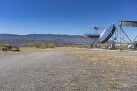 two very large satellite antennas with mountains in the background in a desert area by an open space road