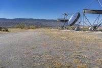 two very large satellite antennas with mountains in the background in a desert area by an open space road