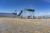 two very large satellite antennas with mountains in the background in a desert area by an open space road