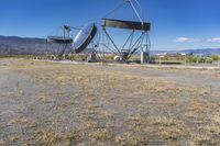 two very large satellite antennas with mountains in the background in a desert area by an open space road