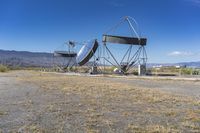 two very large satellite antennas with mountains in the background in a desert area by an open space road