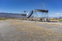 two very large satellite antennas with mountains in the background in a desert area by an open space road