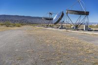 two very large satellite antennas with mountains in the background in a desert area by an open space road