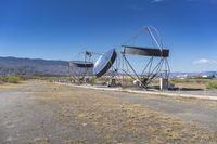 two very large satellite antennas with mountains in the background in a desert area by an open space road