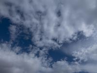 two men fly a kite on the beach during day time with low clouds overhead overhead