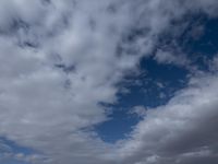 two men fly a kite on the beach during day time with low clouds overhead overhead