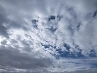 two men fly a kite on the beach during day time with low clouds overhead overhead