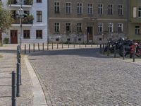 two men are walking down the cobblestone street with scooters and mopeds