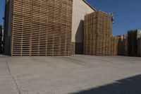 two men walk around with pallets stacked behind them in the sun next to a warehouse