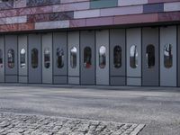two people standing in front of a glass building on a brick walkway between two rows of doors