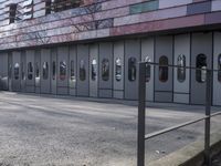 two people standing in front of a glass building on a brick walkway between two rows of doors