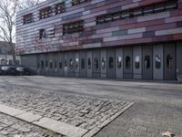 two people standing in front of a glass building on a brick walkway between two rows of doors