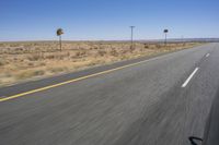 two people riding their bikes down the middle of an empty road in a desert landscape