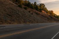 two people ride down the road on a motorcycle at sunset, passing by trees and hills