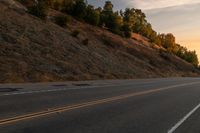 two people ride down the road on a motorcycle at sunset, passing by trees and hills