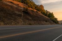 two people ride down the road on a motorcycle at sunset, passing by trees and hills